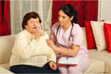 An elderly drinking a glass of water and assisted by a nurse